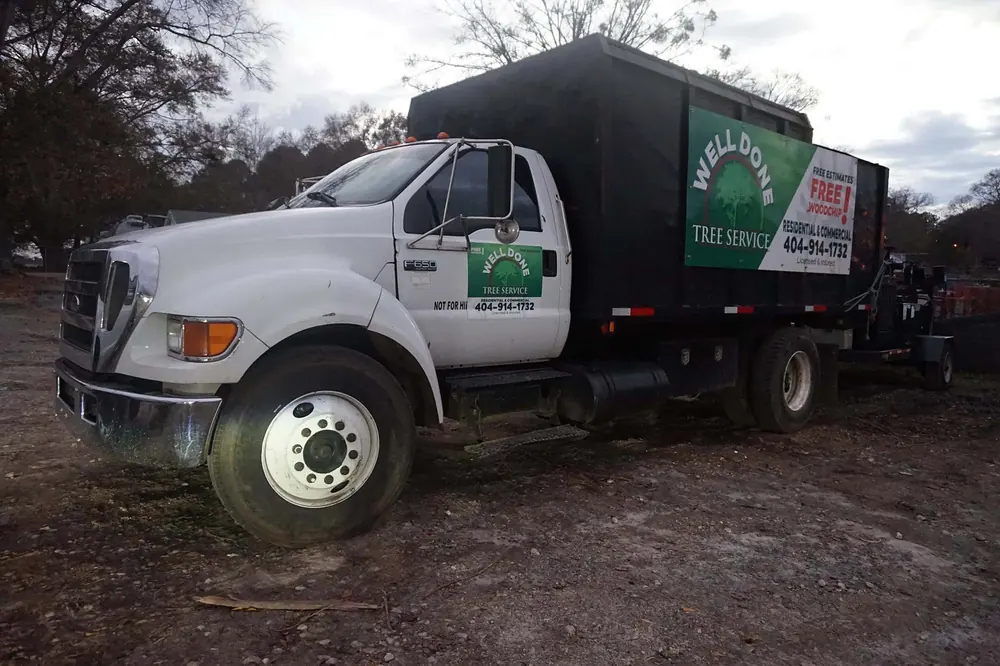 Branded Well Done Tree Service chip truck at the yard at the end of a work day